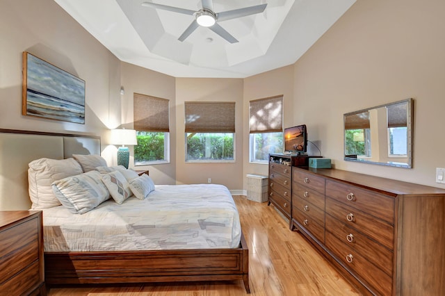 bedroom with ceiling fan, a raised ceiling, and light wood-type flooring