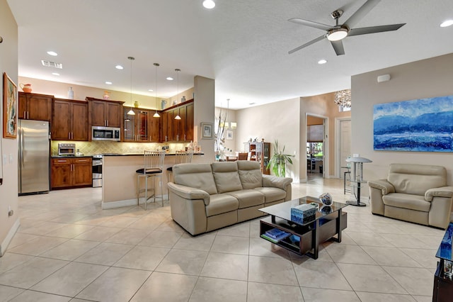 living room with light tile patterned floors, ceiling fan with notable chandelier, and a textured ceiling