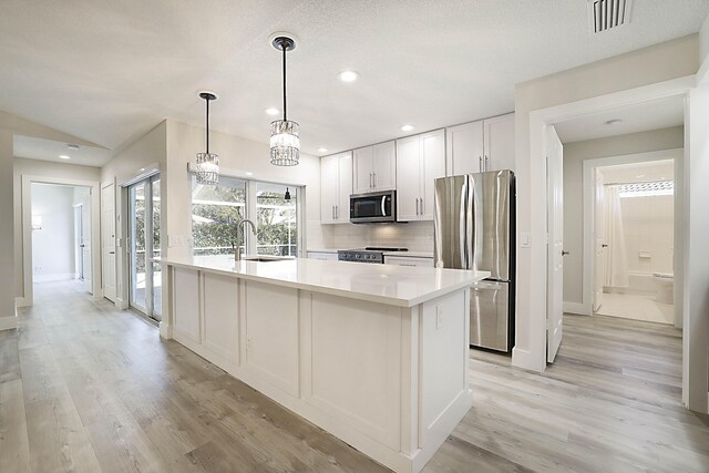 kitchen with light wood-type flooring, stainless steel appliances, pendant lighting, a center island with sink, and white cabinets