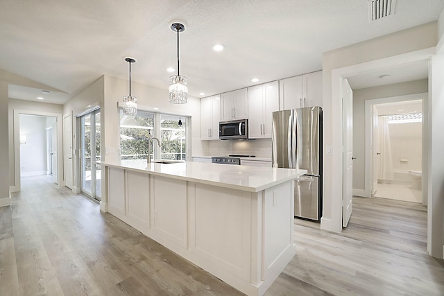 kitchen with pendant lighting, sink, appliances with stainless steel finishes, white cabinetry, and an island with sink