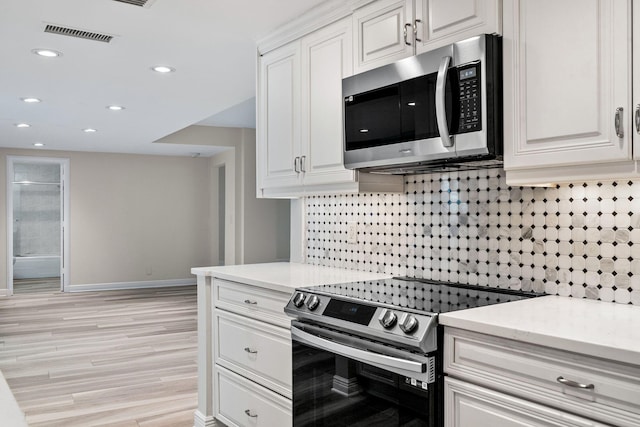 kitchen featuring white cabinetry, appliances with stainless steel finishes, light wood-type flooring, and decorative backsplash