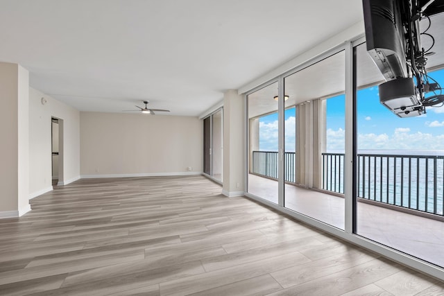 unfurnished room featuring a water view, expansive windows, ceiling fan with notable chandelier, and light hardwood / wood-style floors