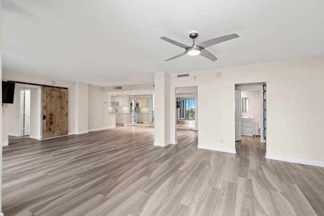 unfurnished living room with a barn door, ceiling fan, and light hardwood / wood-style flooring