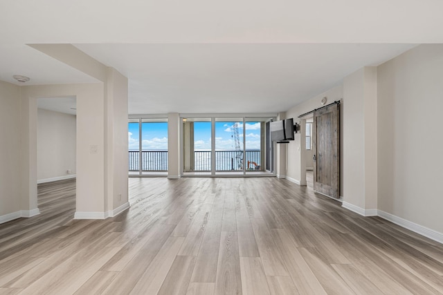 unfurnished living room featuring a barn door, a wall of windows, and light hardwood / wood-style floors