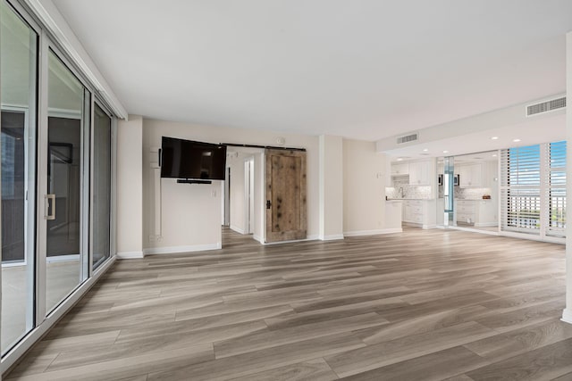 unfurnished living room featuring a barn door and light hardwood / wood-style flooring