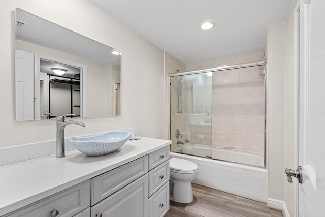 full bathroom featuring vanity, hardwood / wood-style flooring, bath / shower combo with glass door, and toilet