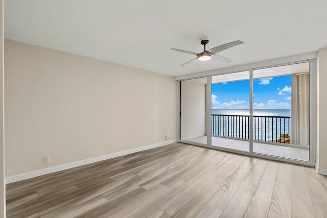 empty room featuring a water view, a wall of windows, ceiling fan, and hardwood / wood-style floors