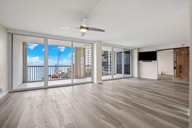 unfurnished living room with a water view, ceiling fan, hardwood / wood-style flooring, a wall of windows, and a barn door