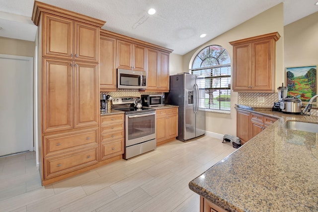 kitchen with sink, stainless steel appliances, dark stone countertops, a textured ceiling, and lofted ceiling