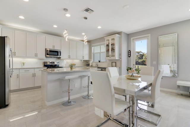 kitchen with white cabinets, stainless steel appliances, a kitchen island, and hanging light fixtures