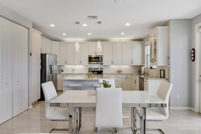 kitchen featuring a center island, light stone countertops, appliances with stainless steel finishes, decorative light fixtures, and a kitchen bar