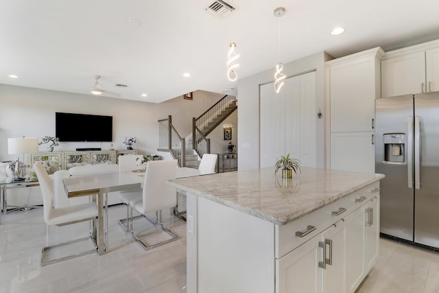 kitchen with light stone countertops, stainless steel fridge, a kitchen island, decorative light fixtures, and white cabinetry