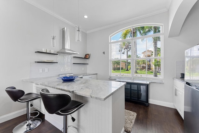 kitchen featuring wall chimney exhaust hood, a kitchen breakfast bar, dark hardwood / wood-style floors, backsplash, and white cabinets