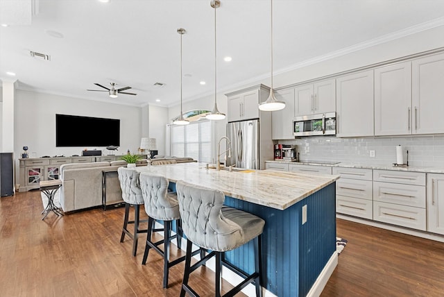 kitchen with ceiling fan, a kitchen island with sink, hanging light fixtures, and stainless steel appliances