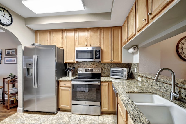 kitchen featuring sink, backsplash, stainless steel appliances, light stone countertops, and light brown cabinets