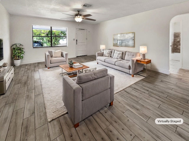 living room with a textured ceiling, light wood-type flooring, and ceiling fan