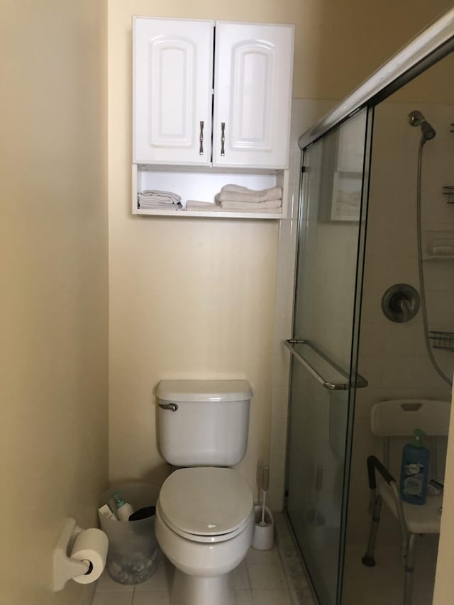 bathroom with tile patterned flooring, toilet, and a shower with door