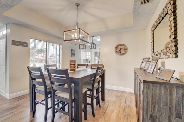 dining area featuring a textured ceiling, light hardwood / wood-style floors, and a tray ceiling