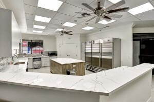 kitchen featuring light stone countertops, a drop ceiling, sink, kitchen peninsula, and a spacious island