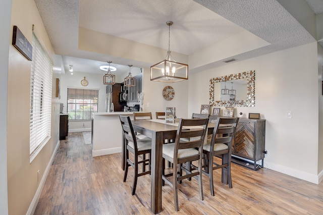 dining space with light wood-type flooring, a textured ceiling, a tray ceiling, and a chandelier