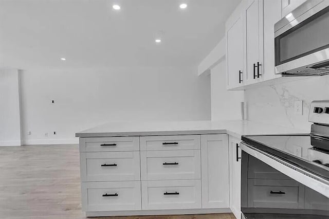 kitchen with white cabinetry, tasteful backsplash, kitchen peninsula, appliances with stainless steel finishes, and light wood-type flooring