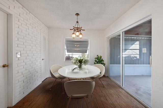 dining area featuring an inviting chandelier, brick wall, wood-type flooring, and a textured ceiling