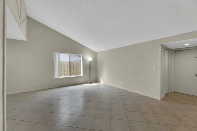 empty room with a textured ceiling, light tile patterned floors, and lofted ceiling