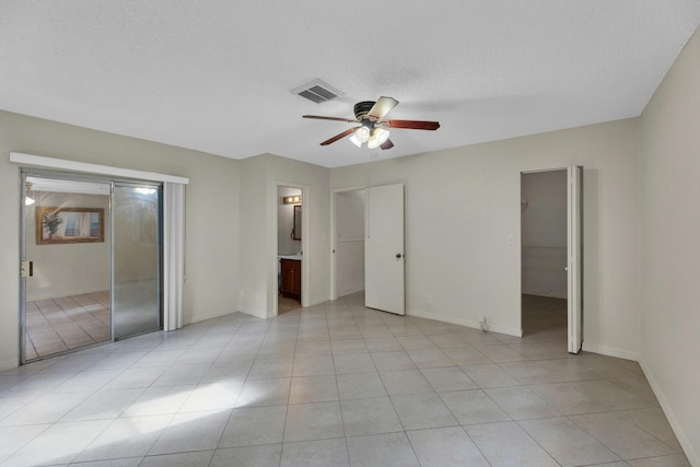 unfurnished bedroom featuring connected bathroom, ceiling fan, light tile patterned floors, and a textured ceiling