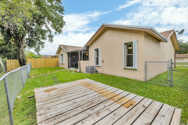 rear view of house with central air condition unit, a wooden deck, a sunroom, and a yard