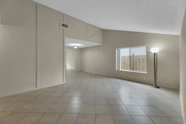 empty room with light tile patterned floors, a textured ceiling, and vaulted ceiling