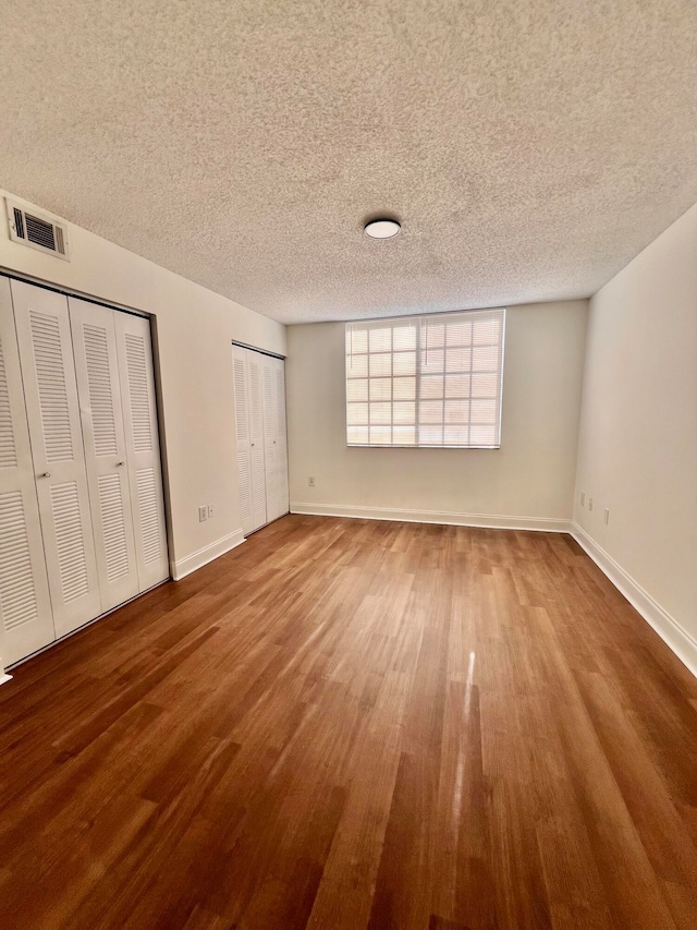 unfurnished bedroom with a textured ceiling, hardwood / wood-style floors, and two closets