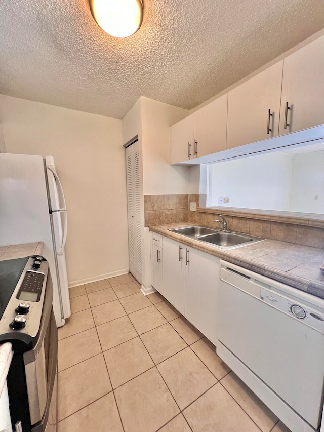 kitchen with sink, light tile patterned floors, a textured ceiling, white appliances, and white cabinets