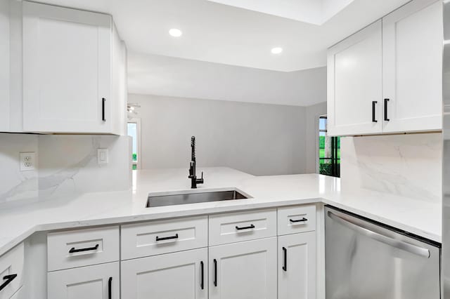 kitchen featuring dishwasher, a peninsula, a sink, and white cabinets