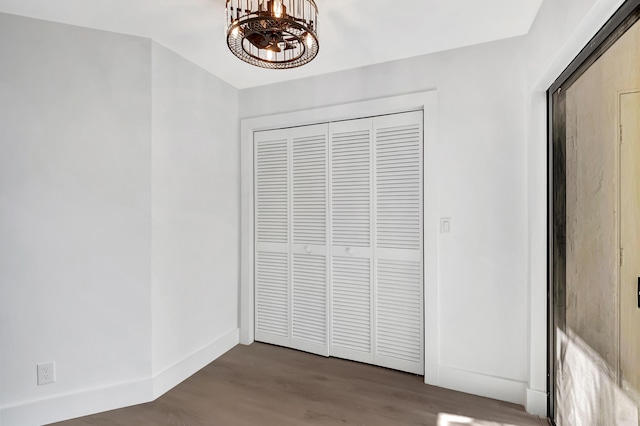 interior space featuring an inviting chandelier, a closet, baseboards, and wood finished floors