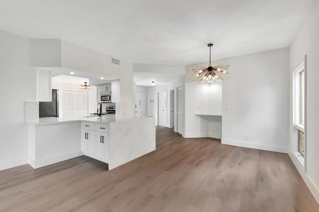 kitchen with wood-type flooring, white cabinetry, kitchen peninsula, and an inviting chandelier