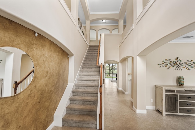 stairs featuring tile patterned floors, crown molding, and a high ceiling