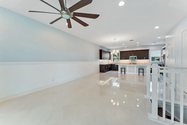 kitchen featuring decorative backsplash, ceiling fan with notable chandelier, dark brown cabinetry, pendant lighting, and a kitchen island