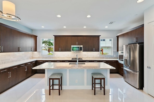 kitchen featuring tasteful backsplash, a kitchen bar, a center island with sink, dark brown cabinets, and appliances with stainless steel finishes