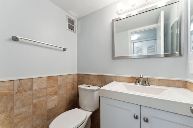 bathroom featuring vanity, toilet, and tile walls