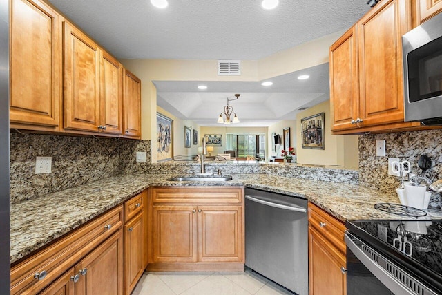 kitchen with sink, a textured ceiling, appliances with stainless steel finishes, a notable chandelier, and light stone counters