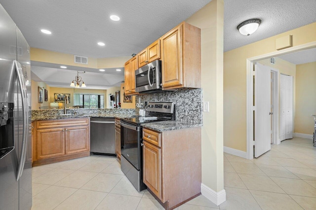 kitchen featuring appliances with stainless steel finishes, a textured ceiling, dark stone counters, and a notable chandelier