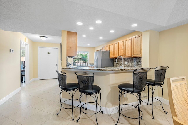 kitchen featuring a textured ceiling, a kitchen breakfast bar, kitchen peninsula, and stainless steel refrigerator with ice dispenser