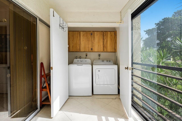 laundry area featuring washing machine and dryer, light tile patterned floors, and cabinets