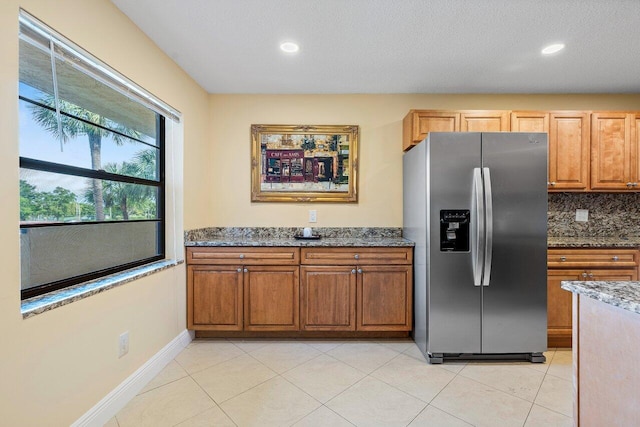 kitchen with stainless steel fridge, backsplash, a textured ceiling, light tile patterned floors, and stone countertops