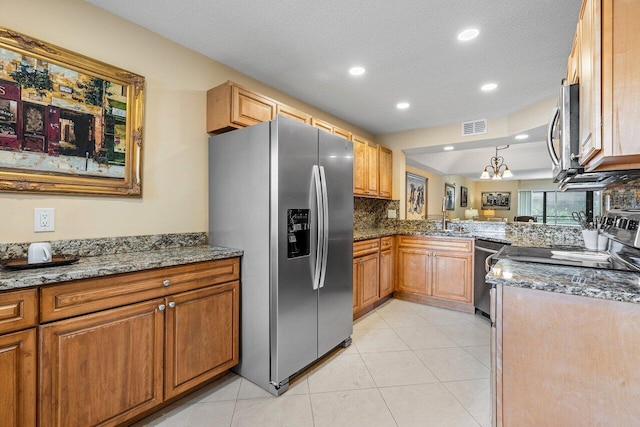 kitchen featuring decorative backsplash, appliances with stainless steel finishes, dark stone counters, a textured ceiling, and an inviting chandelier