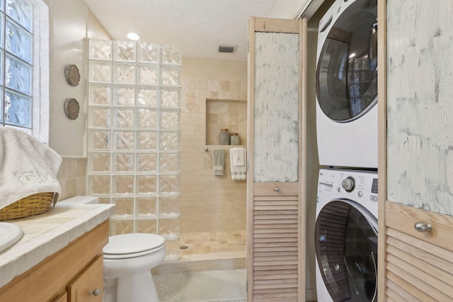 bathroom with a tile shower, vanity, tile walls, toilet, and stacked washer / drying machine