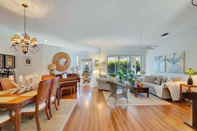 living room featuring ceiling fan with notable chandelier and light wood-type flooring