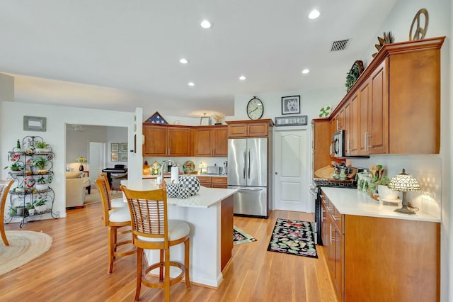 kitchen with decorative backsplash, appliances with stainless steel finishes, a breakfast bar, a center island with sink, and light hardwood / wood-style flooring