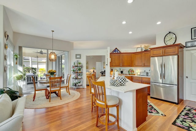 kitchen with ceiling fan, a kitchen breakfast bar, light hardwood / wood-style flooring, stainless steel fridge, and pendant lighting