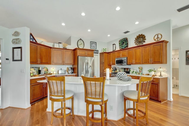 kitchen featuring stainless steel appliances, a kitchen island, light hardwood / wood-style floors, and a breakfast bar area